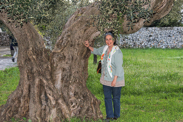 Pamela Sheldon Johns standing next to an olive tree in Puglia.